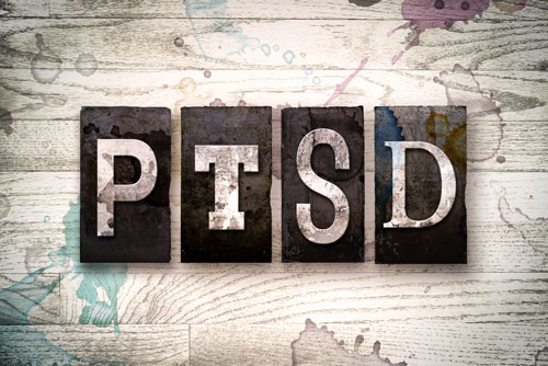 Art carved letters spelling out PTSD on a wooden platform or table.